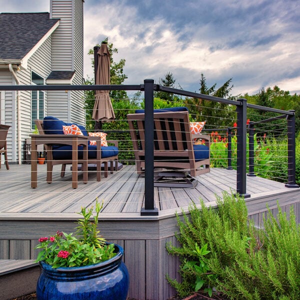 Low-Angle View Of A Custom Grey Composite Deck Featuring Black Metal Cable Railings Vertical Composite Fascia Skirting And Outdoor Lounge Seating With Navy Cushions