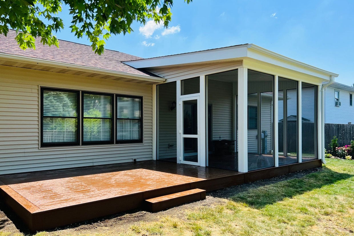 Exterior View Of A Beige House Showing The Seamless Addition When You Build A Sunroom On Your Deck, Connecting To An Open Wood Platform.