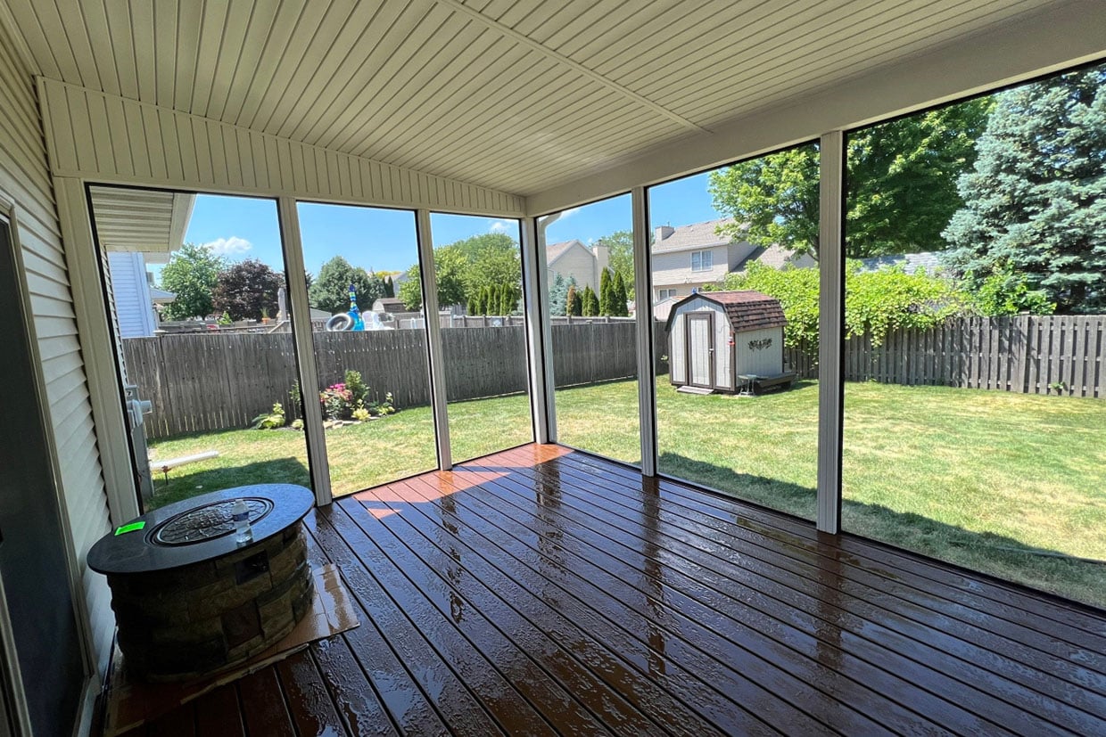 Interior View Of A Spacious Sunroom Enclosure For Deck Featuring Shiny Dark Wood Flooring And Floor-To-Ceiling Screens Overlooking A Backyard.