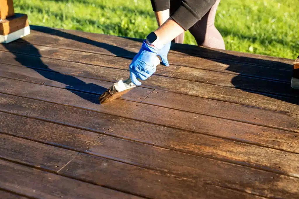 A person applying the best outdoor wood stain and sealer for decks, ensuring a flawless finish and durable protection.