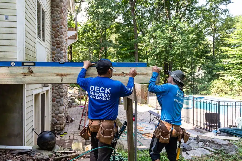 Workers using a level to ensure proper alignment while constructing a deck, choosing a deck builder for a quality installation