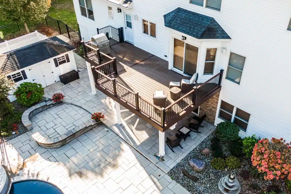 A spacious elevated outdoor deck with a railing, overlooking a paved patio area and lush garden, exemplifying the Patio vs. Porch NJ style.