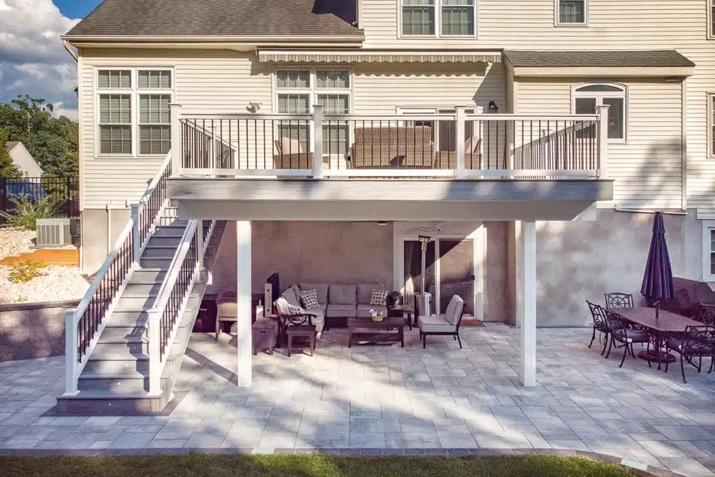 A well-designed porch with white railing and stairs, extending over a paved patio area, showcasing the Build Porch Over Concrete NJ method.
