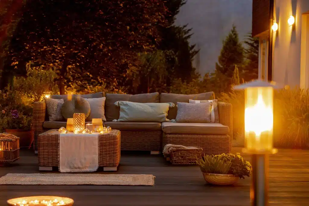 A well-lit patio featuring comfortable seating with pillows, candles, and plants, creating a relaxing outdoor atmosphere.