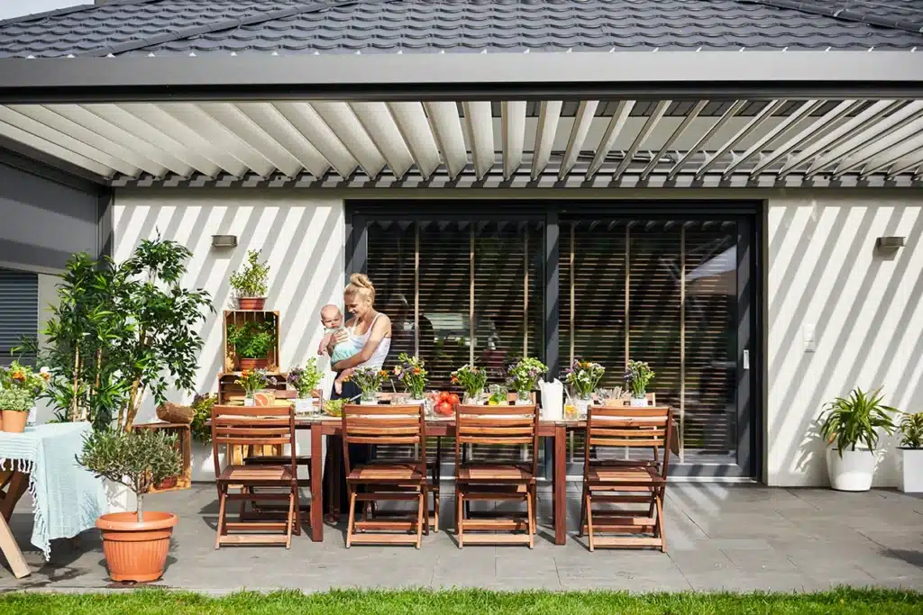 A mother with a child enjoying a louvered roof-covered dining area surrounded by plants and flowers.