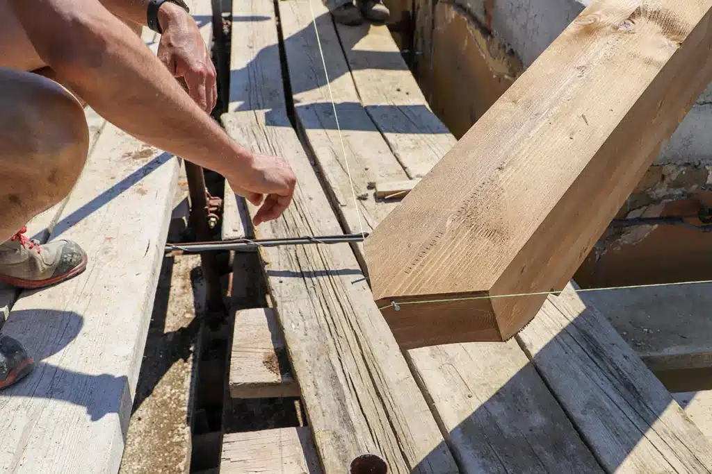 A worker using a level tool to align a timber beam during the deck removal process, ensuring precise measurements.