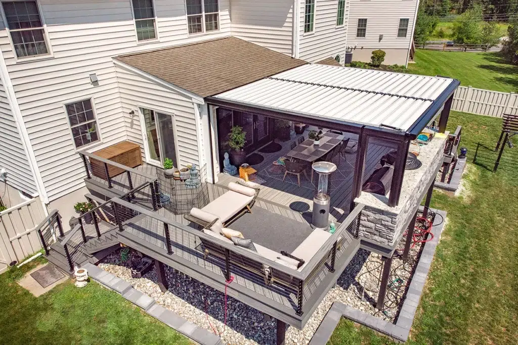 Multi-Level Dark Gray Deck With A Glass-Enclosed Dining Area And Adjustable Louvered Roof, Featuring Superior Eco Friendly Decking.