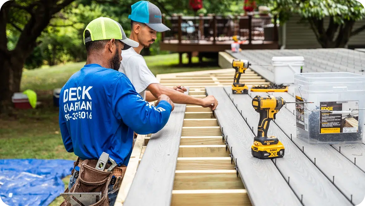 Two Builders Install Gray Composite Decking Boards Using Hidden Fasteners And Yellow Impact Drivers On Wooden Joists.